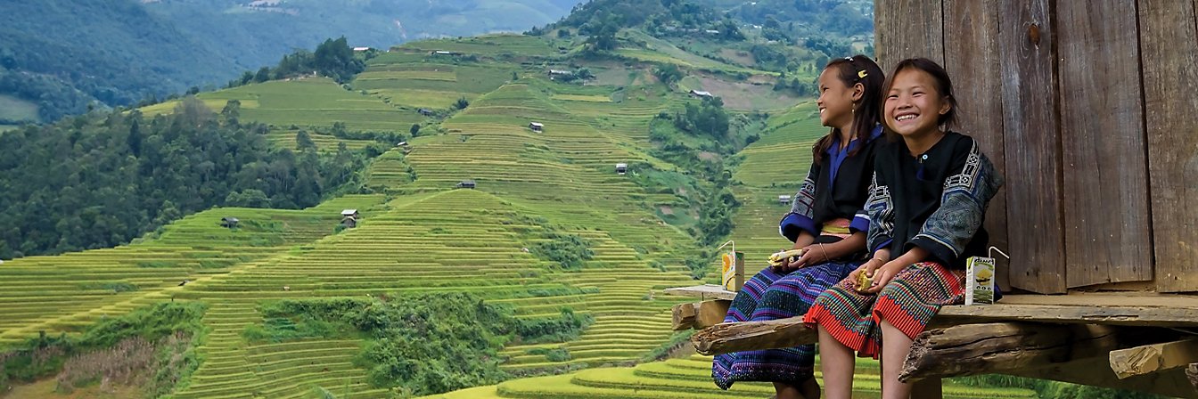 Girls sitting outside wooden house, terrace cultivation in background