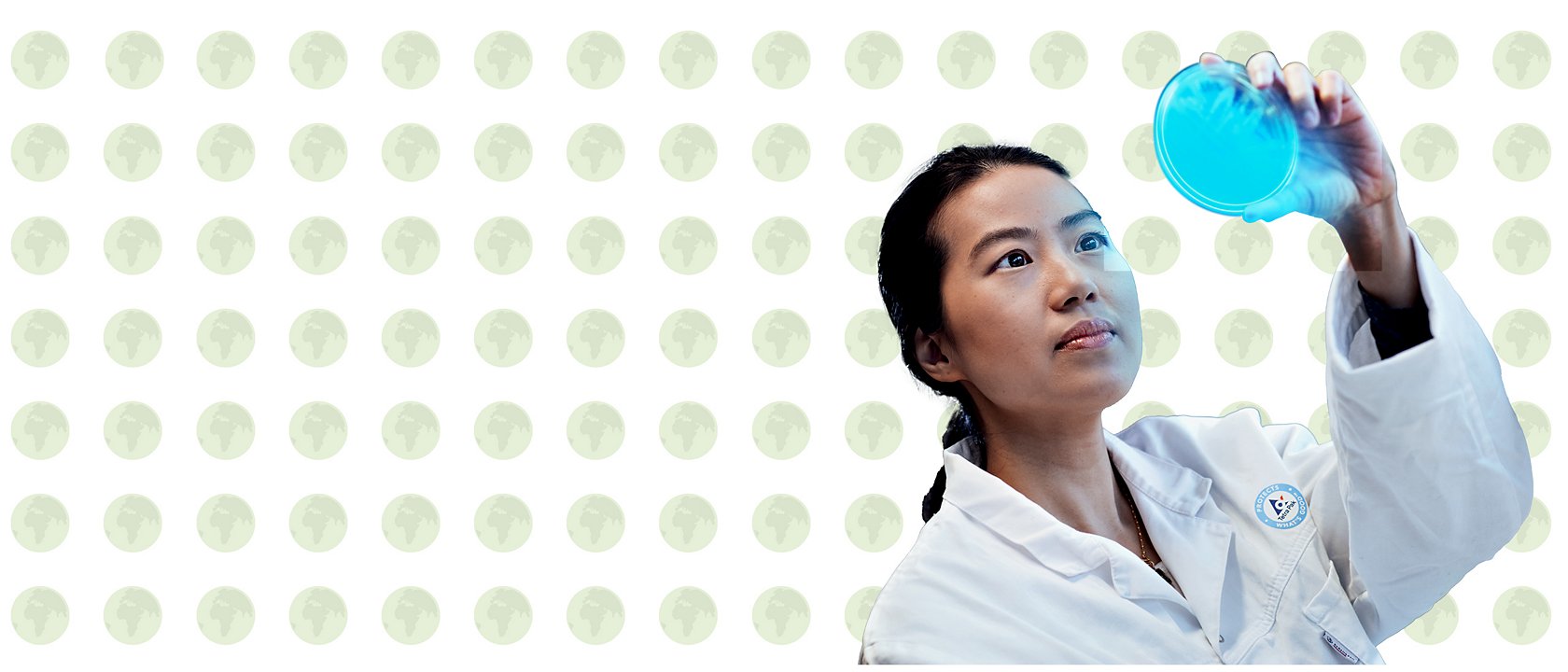 A woman in a lab coat holds an object up to inspect it closely.